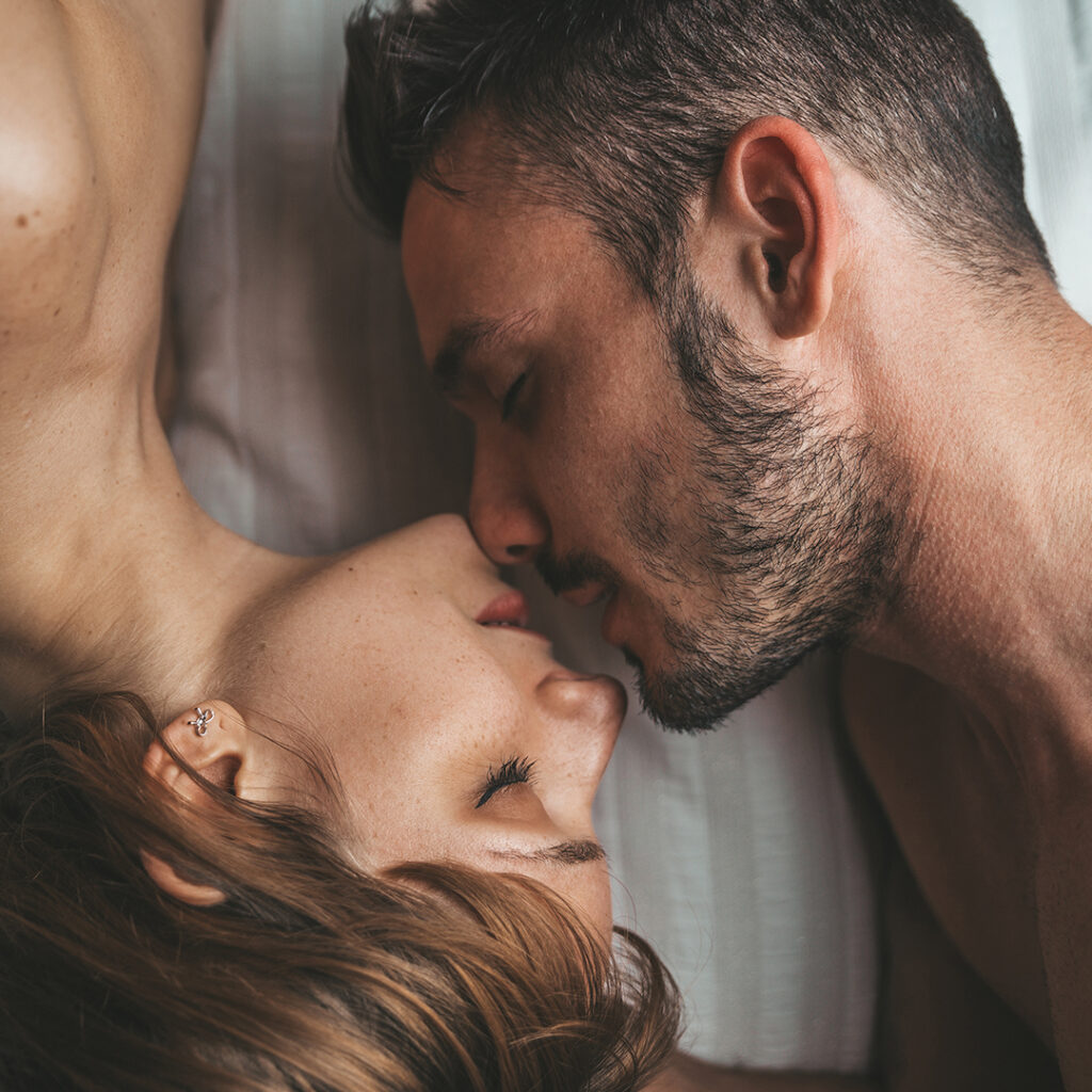 A couple lying in bed, faces close with noses touching chins, displaying happiness and satisfaction. This intimate moment represents the positive impact of Sexual Wellness Stem Cell Treatment on their relationship