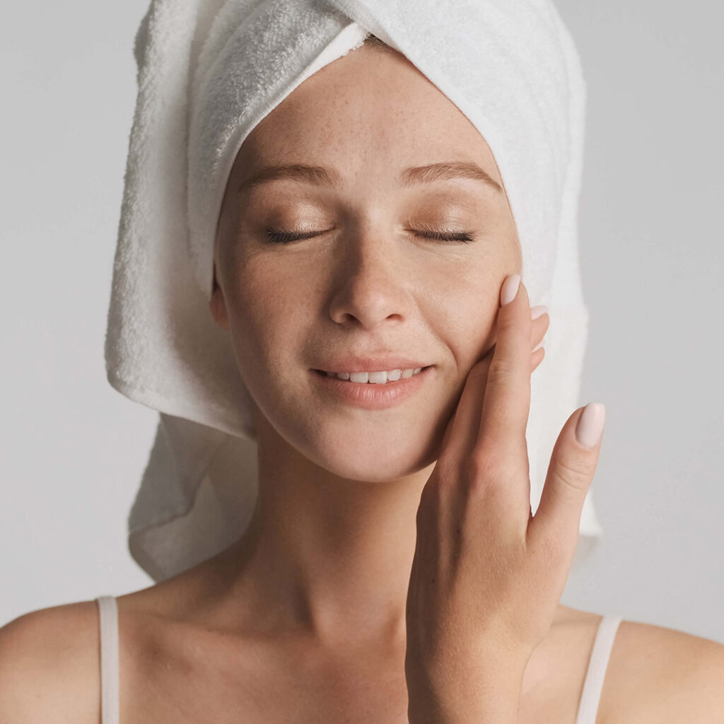 Woman gently touching her face, showcasing the radiant and healthy appearance of her skin as a result of Cosmetic Stem Cell Treatment.